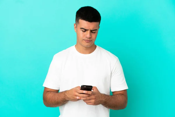 Mladý Pohledný Muž Přes Izolované Modré Pozadí Pomocí Mobilního Telefonu — Stock fotografie
