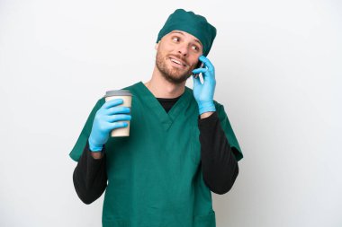 Cerrah Brezilyalı yeşil üniformalı adam beyaz arka planda izole edilmiş. Elinde kahve ve cep telefonu var.