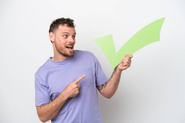 Beyaz arka planda izole edilmiş genç Brezilyalı bir adam elinde bir çek simgesi tutuyor ve onu işaret ediyor.