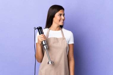 Mor arka planda izole edilmiş el blenderi kullanan Brezilyalı kadın.