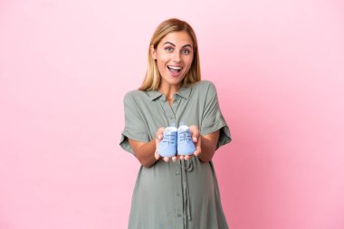 Genç Uruguaylı kadın mavi arka planda izole edilmiş hamile ve bebek paçası tutuyor.