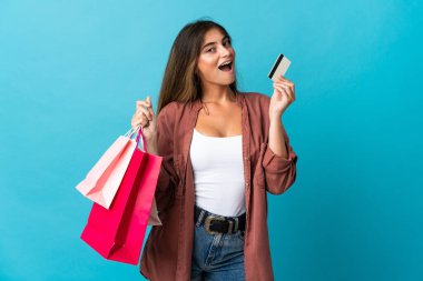 Mavi arka planda izole edilmiş beyaz bir kadın elinde alışveriş çantaları ve bir kredi kartı tutuyor.