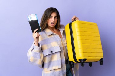 Mor arka planda izole edilmiş beyaz bir kadın. Bavul ve pasaportla tatilde mutsuz.
