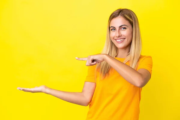 Blonde乌拉圭女孩被隔离在黄色背景下 手掌上有一个想象的复制空间 插入一个广告 — 图库照片