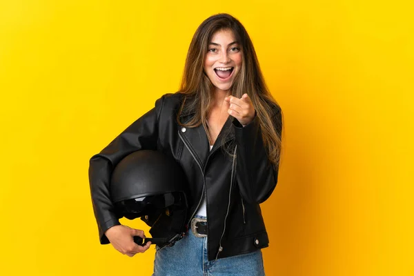 黄色の背景に隔離されたオートバイのヘルメットを持っている女性は驚いて前を指して — ストック写真