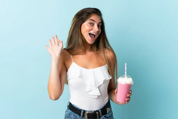 青地に単離されたイチゴミルクシェイクを持つ若い女性幸せな表情で手で塩漬け — ストック写真