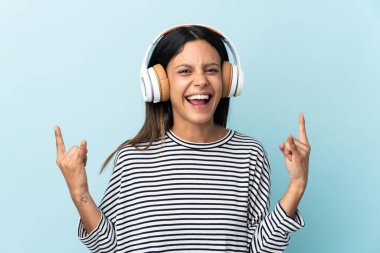 Kafkasyalı kız mavi arka planda izole edilmiş rock hareketleri yapan müzik dinliyor.
