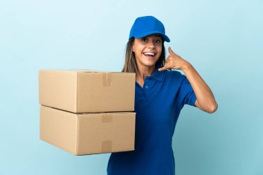 Genç teslimatçı kadın mavi arka planda izole edilmiş, telefon jesti yapıyor. Bana geri dönüş işareti ver.