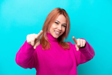 Genç Rus kadın, mavi arka planda izole edilmiş, mutlu bir ifadeyle öne bakıyor.