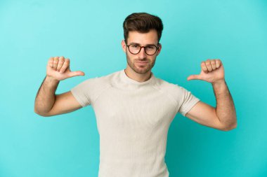 Mavi arka planda soyutlanmış, gururlu ve kendini beğenmiş beyaz, yakışıklı genç bir adam.