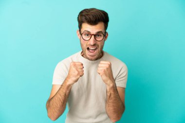 Kafkasyalı yakışıklı adam mavi arka planda izole edilmiş. Kötü bir durum yüzünden hayal kırıklığına uğramış.