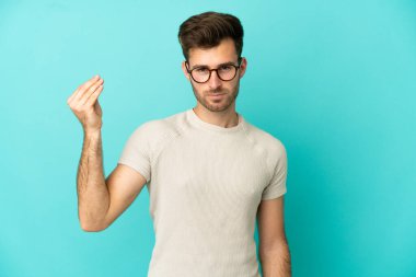 Mavi arka planda izole edilmiş beyaz, yakışıklı bir genç İtalyan jesti yapıyor.