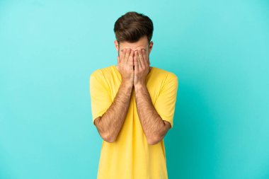 Kafkasyalı yakışıklı genç adam mavi arka planda izole edilmiş, yorgun ve hasta bir ifadeyle.