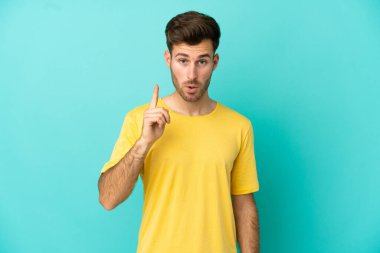 Genç, beyaz, yakışıklı bir adam mavi arka planda izole edilmiş. Çözümü bulmak için parmağını kaldırıyor.