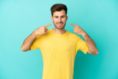 Beyaz tenli yakışıklı adam mavi arka planda izole edilmiş bir şekilde baş parmak işareti yapıyor.
