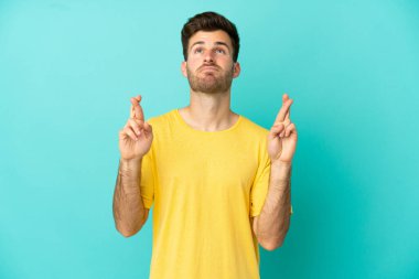 Beyaz tenli yakışıklı adam mavi arka planda izole edilmiş, şans diliyor ve en iyisini diliyor.