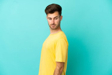 Mavi arka planda soyutlanmış beyaz, yakışıklı genç bir adam. Portre