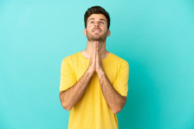 Mavi arka planda izole edilmiş beyaz tenli yakışıklı adam avuç içlerini bir arada tutuyor. İnsan bir şey ister.