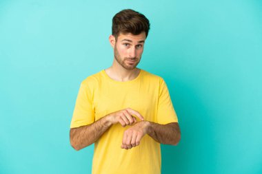 Beyaz tenli yakışıklı adam mavi arka planda izole edilmiş, geç kalma jesti yapıyor.