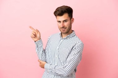Pembe arka planda izole edilmiş genç beyaz yakışıklı adam mutlu ve yukarıya bakıyor.