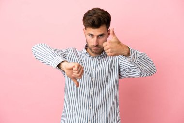 Pembe arka planda izole edilmiş beyaz, yakışıklı bir adam iyiye-kötüye işaret yapıyor. Evet ya da hayır arasında kararsız