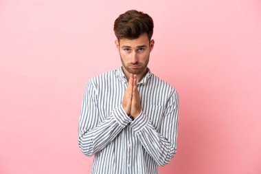 Pembe arka planda izole edilmiş beyaz tenli yakışıklı adam avuç içlerini bir arada tutuyor. İnsan bir şey ister.