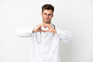 Beyaz arka planda, doktor önlüğü giymiş, elleri olan bir kalp yapan genç bir beyaz adam.