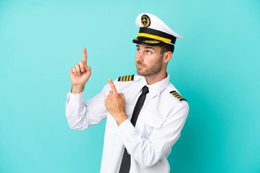 Kafkasyalı uçak pilotu mavi arka planda izole edilmiş işaret parmağıyla işaret etmek harika bir fikir.