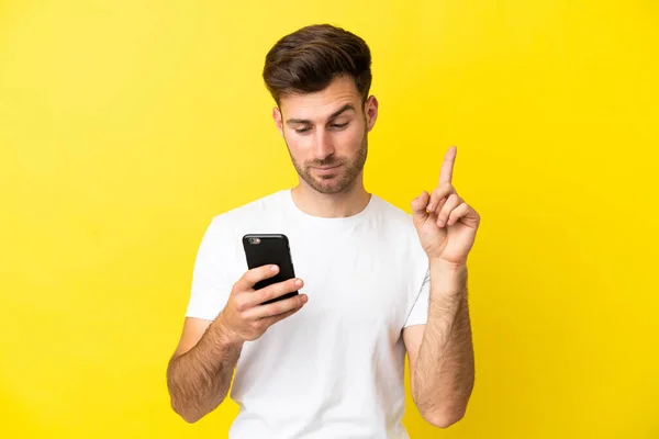 年轻的高加索帅哥 黄种人背景 用手机和举起手指隔离 — 图库照片