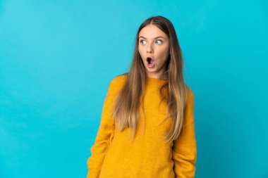 Mavi arka planda izole edilmiş genç Litvanyalı kadın yan tarafa bakarken sürpriz jest yapıyor.