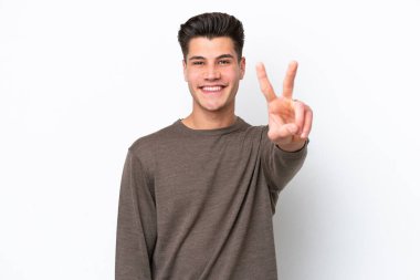 Beyaz fırında izole edilmiş yakışıklı beyaz adam gülümsüyor ve zafer işareti gösteriyor.