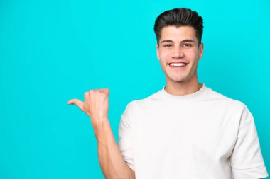 Mavi fırında izole edilmiş yakışıklı beyaz adam bir ürün sunmak için yan tarafı işaret ediyor.