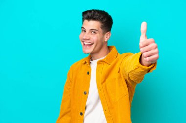 Genç, yakışıklı, beyaz bir adam mavi bakkal bahçesinde izole edilmiş. Başparmakları havada. Çünkü iyi bir şey oldu.