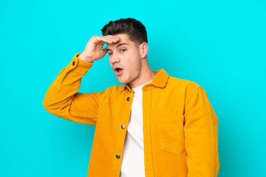 Genç, yakışıklı, beyaz bir adam, mavi bakkalda izole edilmiş. Yan tarafa bakarken sürpriz jest yapıyor.