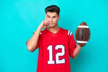 Genç beyaz adam rugby oynuyor. Mavi arka planda izole edilmiş bir şekilde bir fikir düşünüyor.