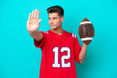 Mavi arka planda ragbi oynayan genç beyaz adam dur hareketi yapıyor ve hayal kırıklığına uğruyor.