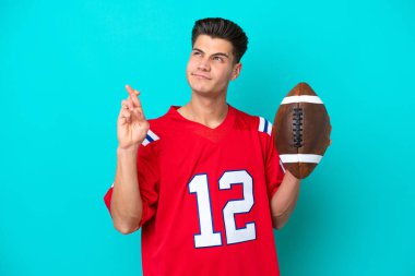 Genç beyaz adam rugby oynuyor. Mavi arka planda izole edilmiş, şans diliyor ve en iyisini diliyor.