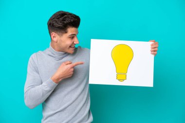 Genç, beyaz bir adam mavi bir bakkal sahasında izole edilmiş. Elinde ampul simgesi olan bir pankart var.