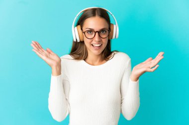 Soyutlanmış mavi arka planda genç bir kadın şaşırmış ve müzik dinliyor.