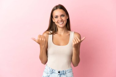 Soyutlanmış pembe bir geçmişi olan genç bir kadın. Baş parmakları havada ve gülümsüyor.