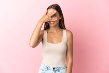 Soyutlanmış pembe arka planda genç bir kadın. Gözleri elleriyle kaplıyor ve gülümsüyor.