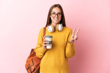 İzole edilmiş pembe arka planda genç bir bayan gülümseyerek ve zafer işareti göstererek