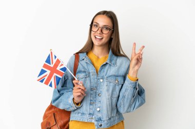 Birleşik Krallık bayrağını izole edilmiş beyaz arka planda tutan genç İspanyol kadın gülümsüyor ve zafer işareti gösteriyor.