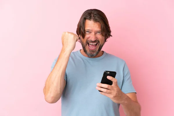 用手机和做胜利手势隔离在粉色背景下的高个子男人 — 图库照片