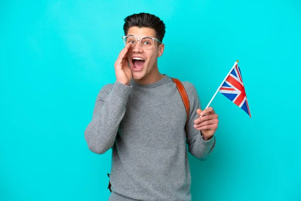 驚きとショックを受けた表情で青い背景に隔離された英国の旗を持つ若い白人男性 — ストック写真