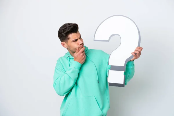 stock image Young handsome caucasian man isolated on white bakcground holding a question mark icon and having doubts