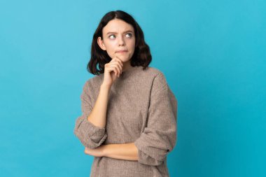 Genç Ukraynalı kız mavi arka planda izole edilmiş. Şüpheleri ve düşünceleri var.