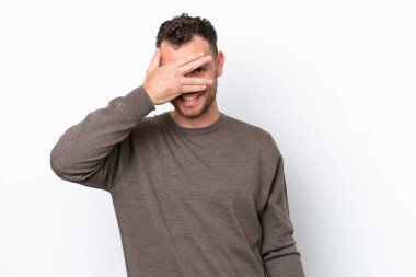 Genç Brezilyalı bir adam beyaz arka planda izole edilmiş gözleri elleriyle kaplıyor ve gülümsüyor.