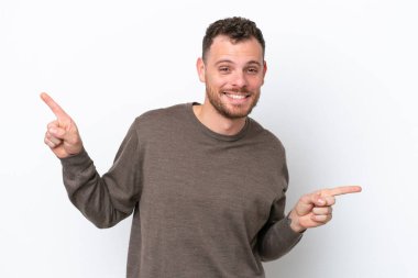 Beyaz arka planda izole edilmiş genç Brezilyalı adam parmak uçlarını işaret ediyor ve mutlu.