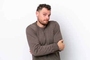 Genç Brezilyalı bir adam beyaz arka planda izole edilmiş. Omuzlarını kaldırırken şüpheyle hareket ediyor.